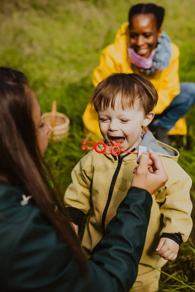enfant en exterieur qui fait des bulles avec son accompagnatrice de la creche